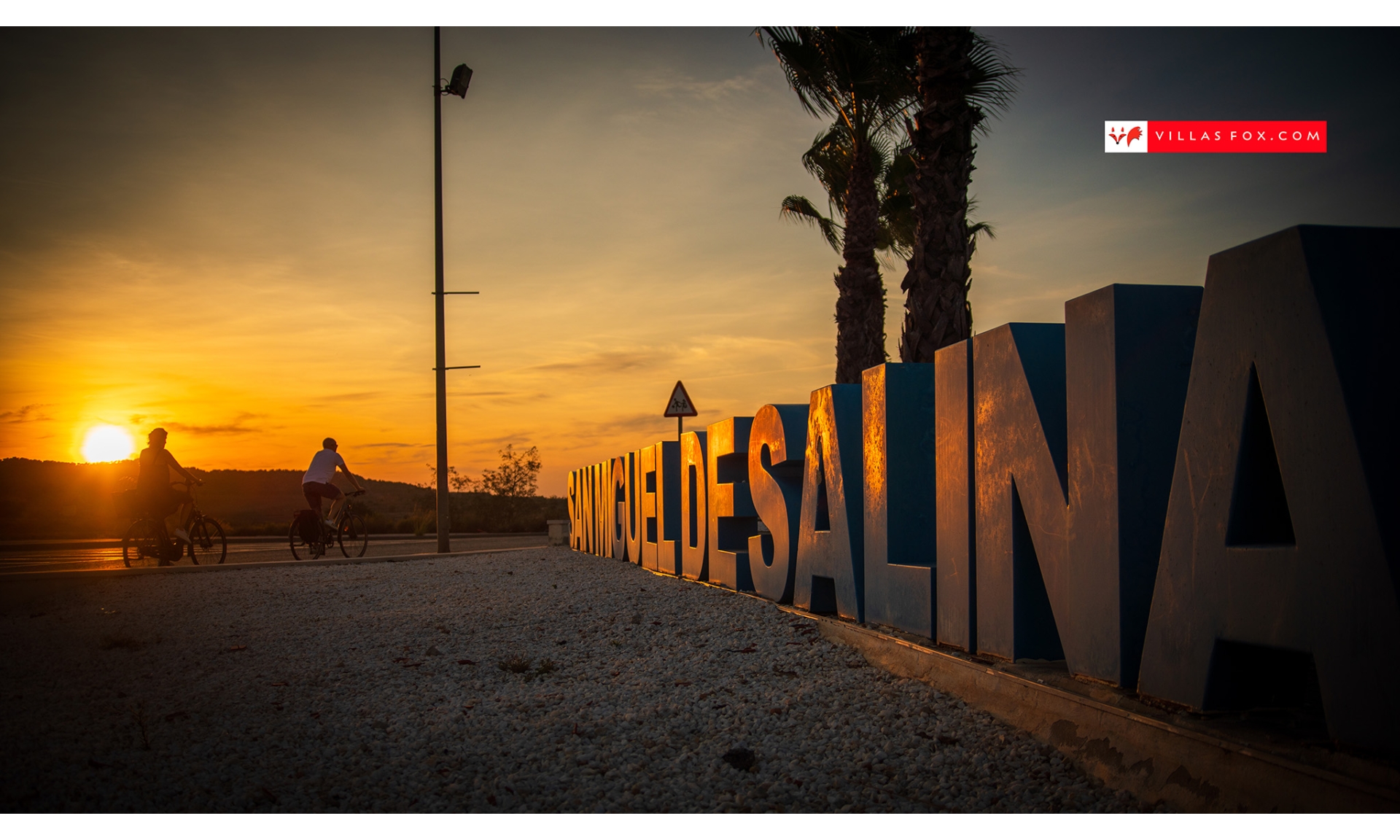 1568_san_miguel_de_salinas_cyclists_and_town_sign_at_sunset