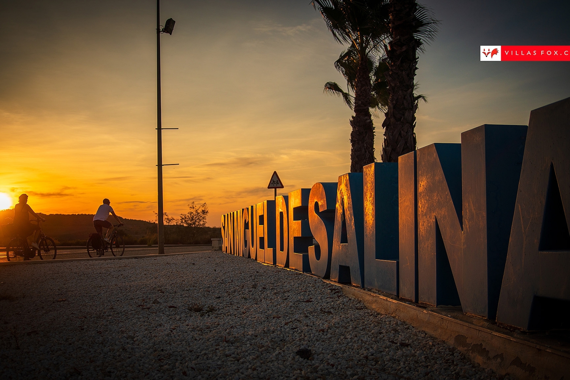 San Miguel de Salinas cyclists and town sign at sunset - copia